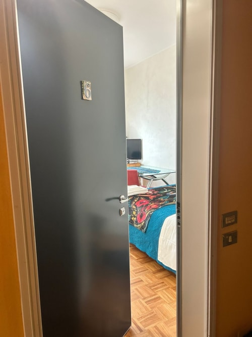 Open door to bedroom in Villa Marisa apartment, Pavia. Blue bedding, wooden floor, desk visible inside.