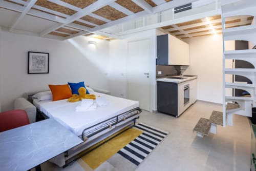 Moderno loft studio a Milano con letto, angolo cottura, tappeto rigato e dettagli in legno a vista presso Solumnia