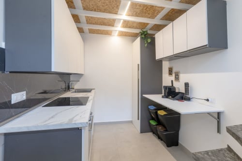 Cucina moderna con piano in marmo, mobili scuri, pensili bianchi, soffitto in sughero, tavolo da pranzo e acciaio inox