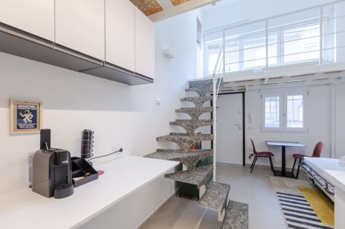 Moderna cucina con zona pranzo in loft a Milano con scala, banconi bianchi, elettrodomestici e vista sulla città attraverso ampie finestre