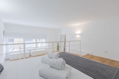 Camera da letto in loft moderno con soppalco, vista sulla città, asciugamani arrotolati sul letto, pavimenti in legno a Milano