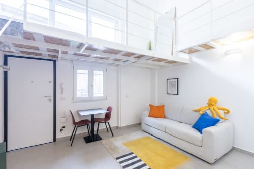 Luminoso loft urbano a Milano con divano bianco, accenti gialli, zona pranzo e spazio lavoro in mezzanino