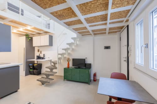 Vini Urban Loft Milano: Moderno appartamento open-plan con cucina, zona pranzo, mobile verde e scala verso il soppalco