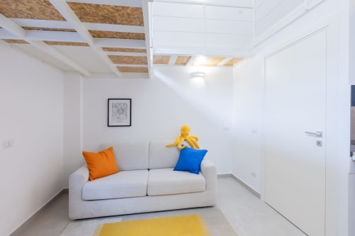 Moderno soggiorno con divano grigio, cuscini colorati e dettagli in legno al soffitto nel loft urbano di Solumnia Milano