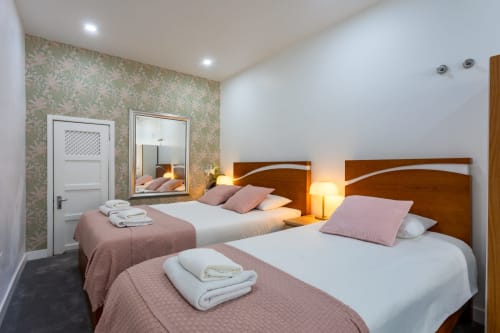 Twin beds with wooden headboards in Estúdio Casal + 1 apartment at Lisbon Poets Inn hostel, featuring pink bedding and city