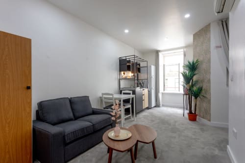 Modern studio apartment at Lisbon Poets Inn hostel with dark sofa, wooden tables, kitchenette, and city view window