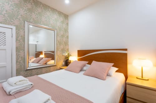 Cozy studio bedroom at Lisbon Poets Inn with wooden headboard, pink pillows, patterned wallpaper and mirror