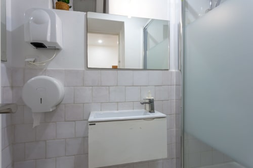 Modern bathroom with white tiles, sink vanity, mirror, and paper towel dispenser at Lisbon Poets Inn hostel in Lisboa