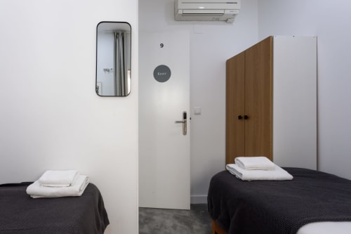 Twin bedroom at Lisbon Poets Inn hostel with two black beds, white linens, mirror, AC unit, and wooden wardrobe