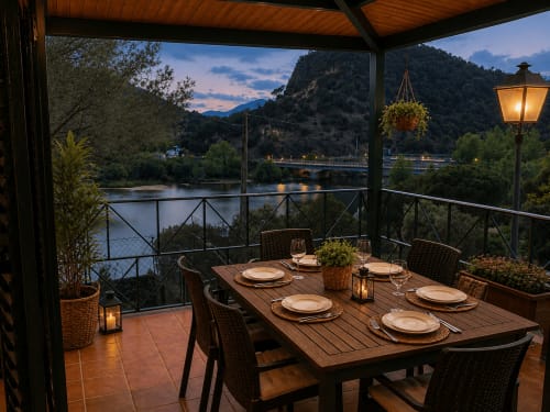 Elegante comedor lacustre bajo terraza cubierta en Las Casitas de Noe, Layos, con vistas al río y montañas al atardecer