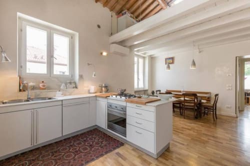 Cucina e zona pranzo open-plan moderna in appartamento a Verona con mobili bianchi, travi in legno e pavimenti in legno