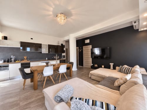 Modern open-plan apartment in Verona with kitchen, dining area, and living room featuring black accent wall and beige sofa