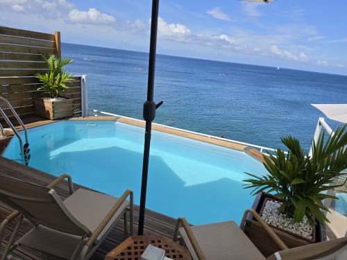 Piscine à débordement turquoise surplombant la mer des Caraïbes à Clémara Evasion en Martinique, avec chaises longues et décor tropical