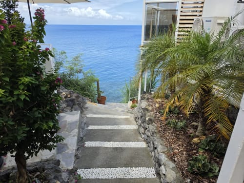 Escalier en pierre menant à la terrasse avec vue mer du gîte Clémara Evasion en Martinique, bordé de plantes tropicales et palmiers