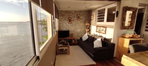 Spacieux salon de cottage à Clémara Evasion avec vue mer, canapé noir, TV écran plat, mur en briques et style côtier
