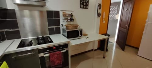 Cuisine moderne avec appareils en acier inoxydable, plans de travail blancs et murs d'accent orange au gîte Clémara Evasion
