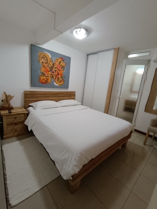 Chambre moderne à Clémara Evasion Martinique avec lit en bois, linge blanc et œuvres d'art abstraites