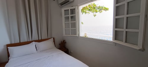 Chambre lumineuse avec vue sur mer à Clémara Evasion, Martinique. Lit double, draps blancs, fenêtres ouvertes sur l'océan