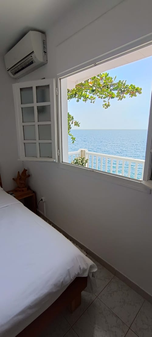 Chambre lumineuse avec vue sur mer, lit blanc, climatisation et balcon donnant sur l'océan à Clémara Evasion