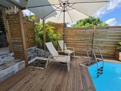 Terrasse de l'appartement Clémara Evasion Oasis à Schœlcher avec chaise longue, parasol et piscine privée vue tropicale