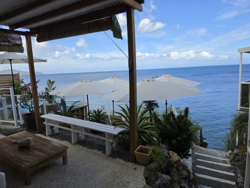 Terrasse Clémara Evasion avec vue sur mer, banc blanc, parasols, plantes tropicales surplombant l'océan de la Martinique