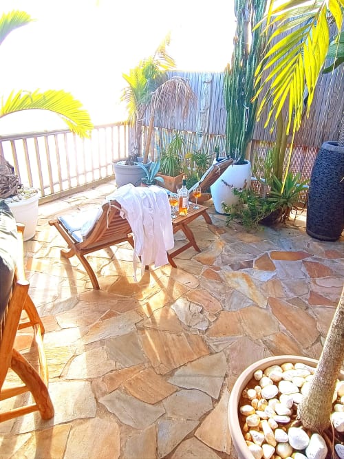 Terrasse ensoleillée à Clémara Evasion en Martinique avec chaise longue, palmiers, patio en pierre et vue sur mer