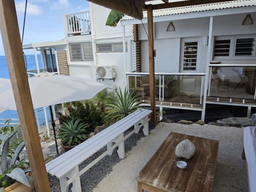 Terrasse de l'appartement Balisier à Clémara Evasion, Martinique avec vue mer, table en bois, plantes et garde-corps blanc moderne