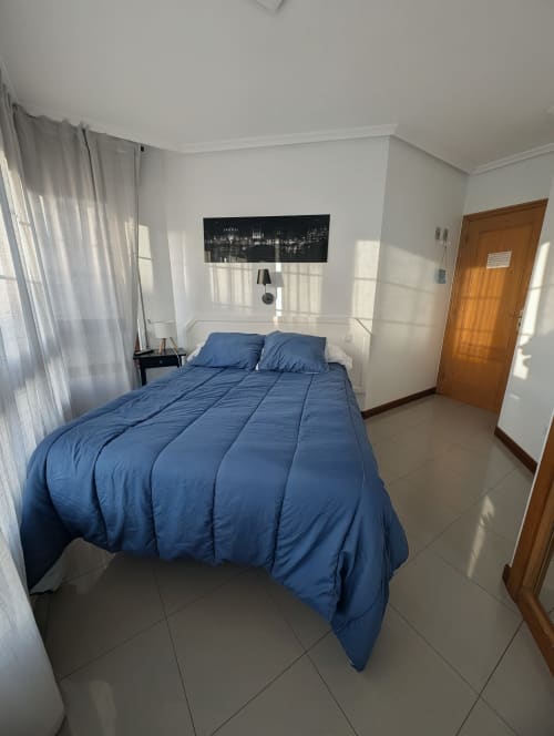 Dormitorio moderno con ropa de cama azul en Alojamiento La Ballena BnB de Santoña, piso de baldosas y vista al monumento emblemático