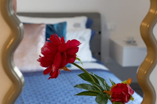 Red peonies in bedroom at Pescara INN sea view apartment with bed and blue linens in background
