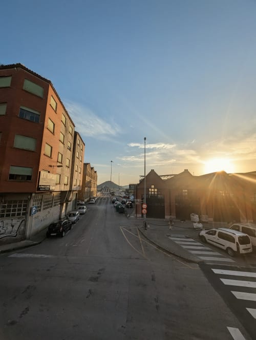 Sunset street view of Santoña with brick buildings, parked cars, and coastal hills at La Ballena BnB