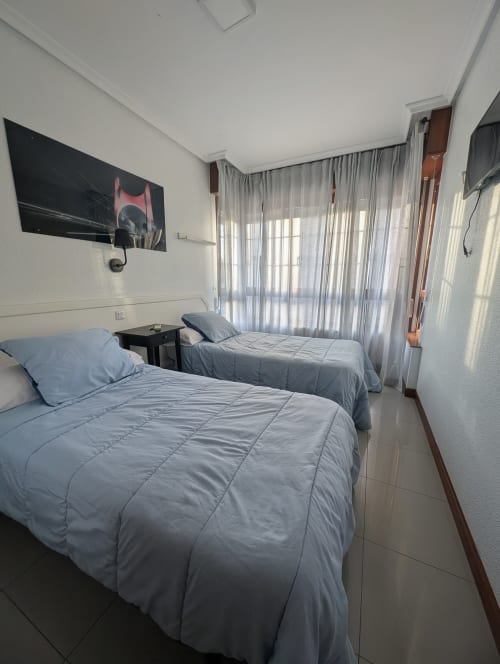 Dormitorio doble con colchas azules en La Ballena B&B en Santoña, España, con TV y cortinas translúcidas