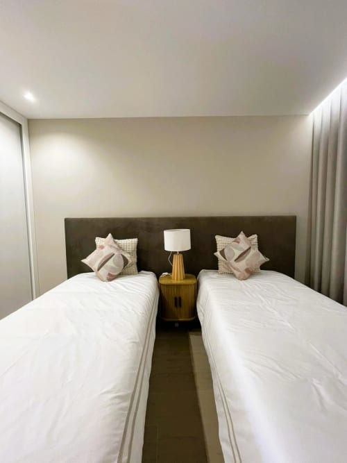 Camas geminadas com almofadas decorativas, cabeceira escura e luminária dourada no apartamento Villa Sotto Mayor, Figueira da Foz