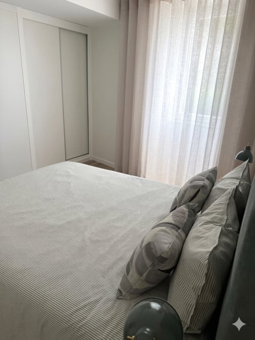 Quarto moderno da Villa Sotto Mayor, Figueira da Foz, com cama, almofadas às riscas, cortinas translúcidas e guarda-roupa corrediço.