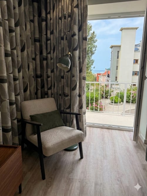 Varanda moderna da Villa Sotto Mayor com vista para o mar, cortinas bege estampadas, cadeira estilo anos 50 e cidade litorânea de