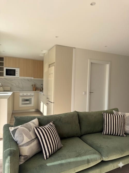 Sala de estar moderna com sofá verde e almofadas listradas, cozinha integrada com armários creme na Villa Sotto Mayor, Figueira