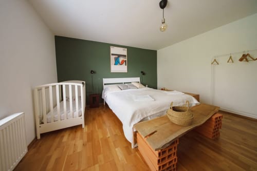 Bright modern bedroom at Kmetija Pečnik with green accent wall, queen bed, crib, wooden floors and natural light