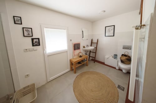 Bright bathroom at Kmetija Pečnik with toilet, sink, circular jute rug, and wooden furnishings