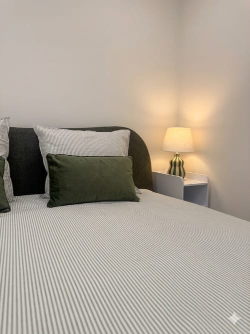 Quarto aconchegante na Villa Sotto Mayor em Figueira da Foz com roupa de cama listrada, almofada verde-oliva e luminária aquecida na cabeceira