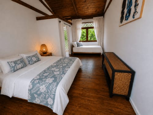 Chambre spacieuse à Fare Tihi Moana à Uturoa avec deux lits, poutres en bois et vue sur jardin tropical