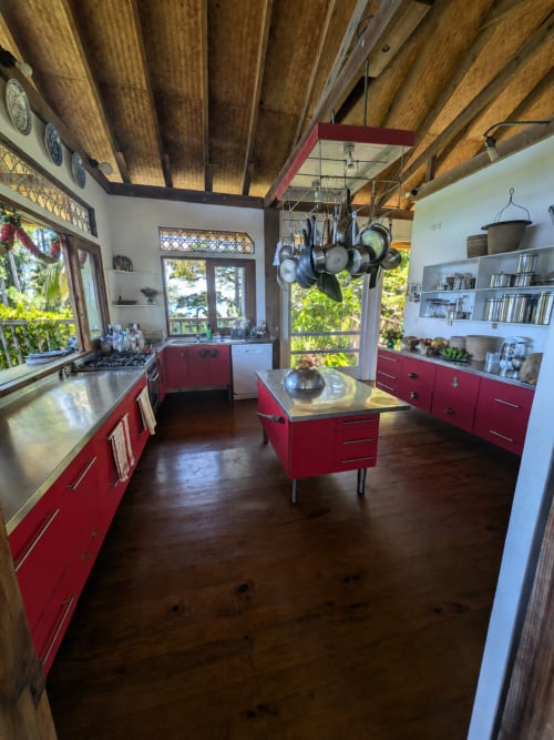 Cuisine moderne et lumineuse avec armoires rouges, poutres en bois, îlot et batterie suspendue à Fare Tihi Moana, Uturoa