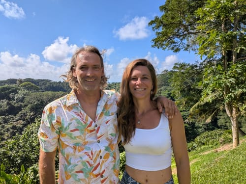 Deux clients souriants en extérieur à la pension Fare Tihi Moana en Uturoa, Polynésie française, entourés d'une luxuriante végétation tropicale