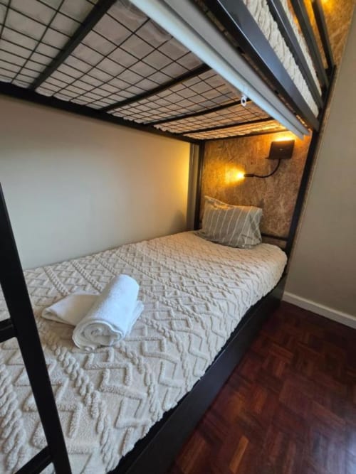 Cama beliche aconchegante na Pousada Mãe Maria em Vila Chã, com roupa de cama branca, toalha enrolada e iluminação ambiente acolhedora