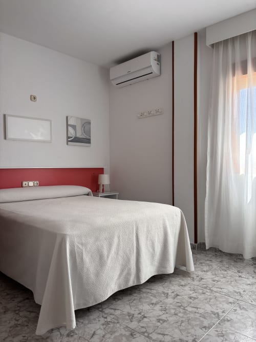 Habitación doble en Hostal Las Dunas con cama blanca, cabecero rojo, aire acondicionado y mobiliario moderno en Cabo de Gata