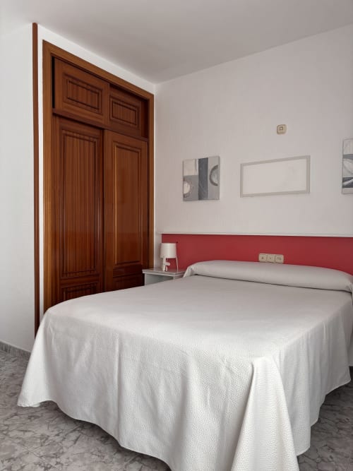 Habitación doble en Hostal Las Dunas, Cabo de Gata, con armario de madera, cama blanca, cabecero rojo y equipamientos modernos