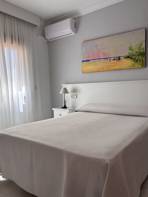 Luminosa habitación doble en Hostal Las Dunas, Cabo de Gata con cama blanca, aire acondicionado, arte marino y vistas al mar