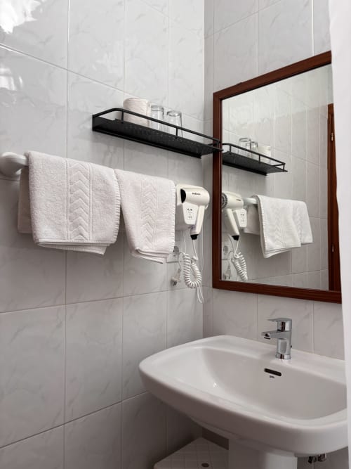 Baño moderno en Hostal Las Dunas con azulejos blancos, lavabo, espejo, toallero y repisa mural en Cabo de Gata