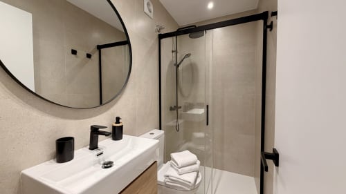 Baño moderno en apartamento Gran Reserva Sea Breeze de Holidays Costa Brava con ducha de cristal, lavamanos blanco y detalles en negro
