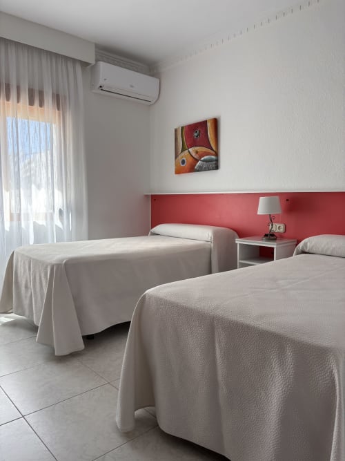 Habitación doble luminosa en Hostal Las Dunas con dos camas, pared roja de acento, aire acondicionado y comodidades modernas en Cabo de Gata