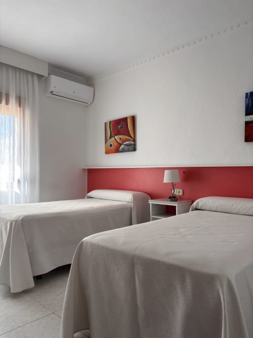 Habitación doble con dos camas en Hostal Las Dunas, Cabo de Gata. Cabecero rojo, aire acondicionado, TV y decoración moderna.