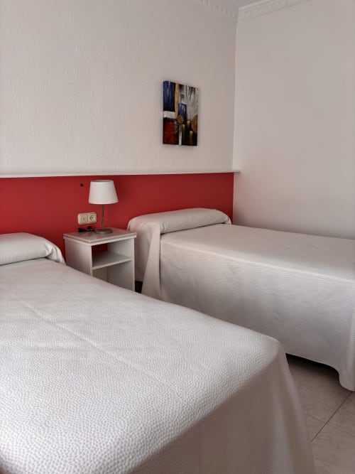 Camas gemelas en habitación luminosa del Hostal Las Dunas, Cabo de Gata, con pared roja y comodidades modernas